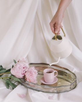 一只手将茶倒入装有粉红色牡丹的托盘中，环境优雅而宁静