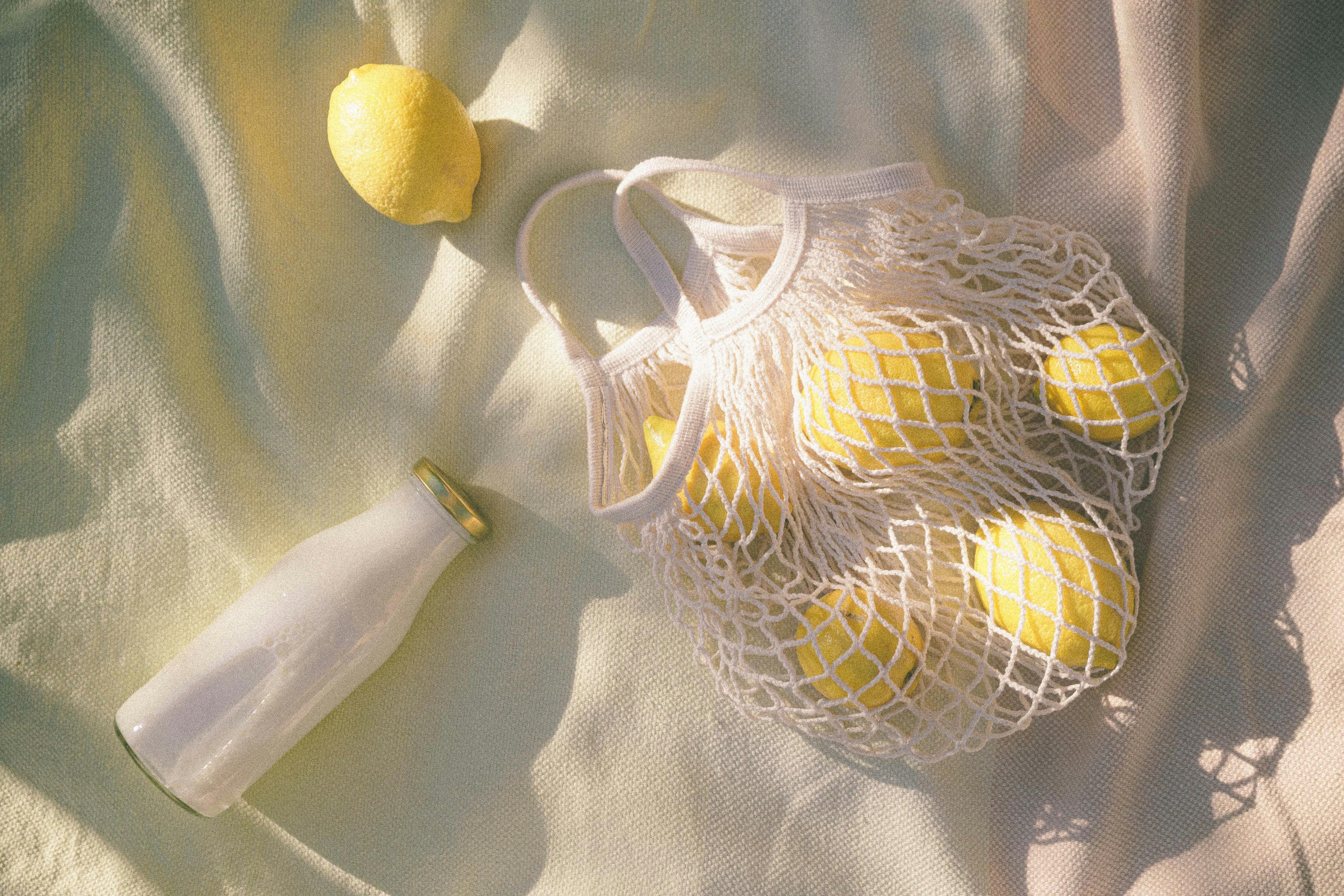 Photograph of a string bag filled with lemons beside a glass bottle, depicting eco-friendly shopping.