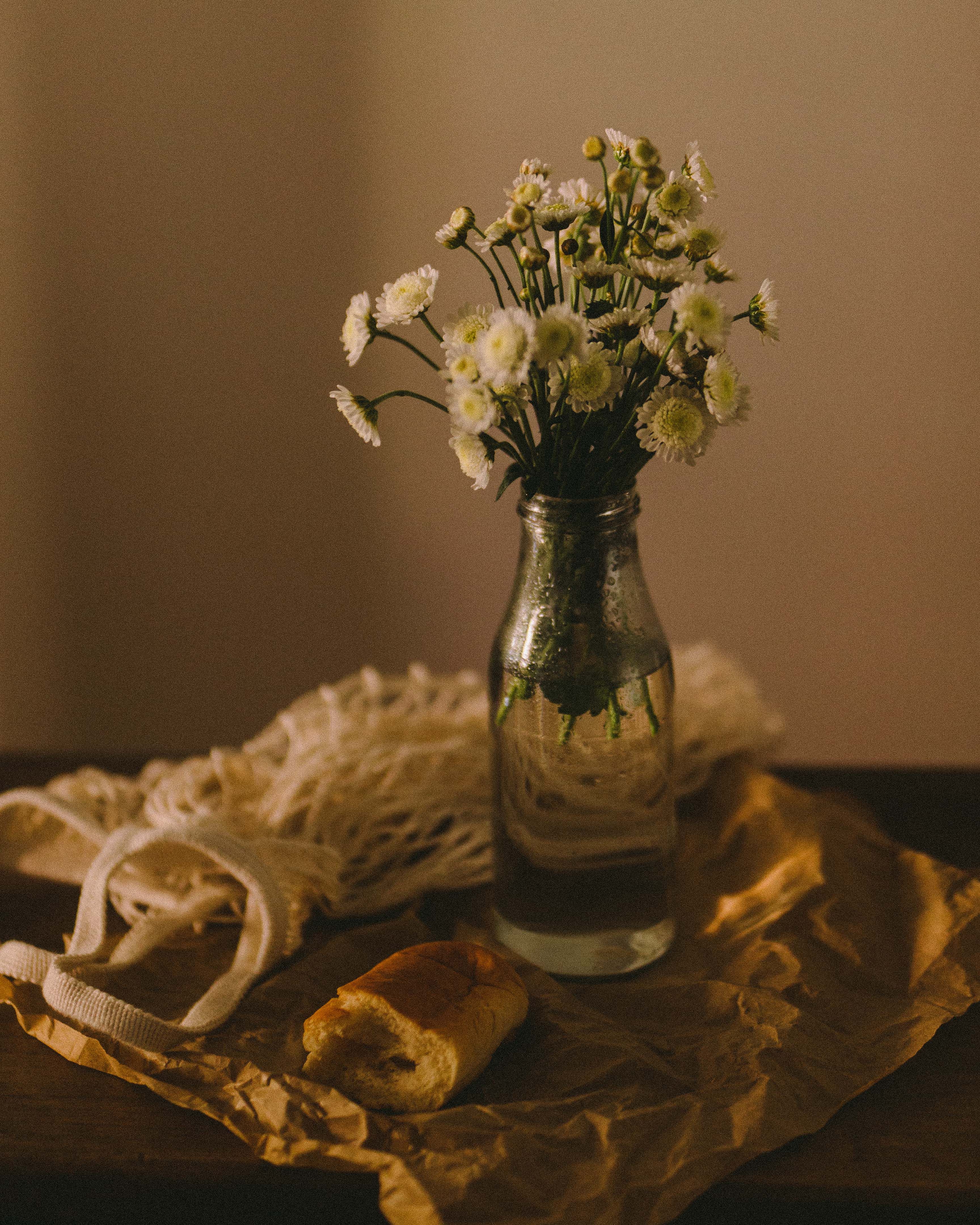 Charming still life of white flowers in glass vase with bread on torn paper.
