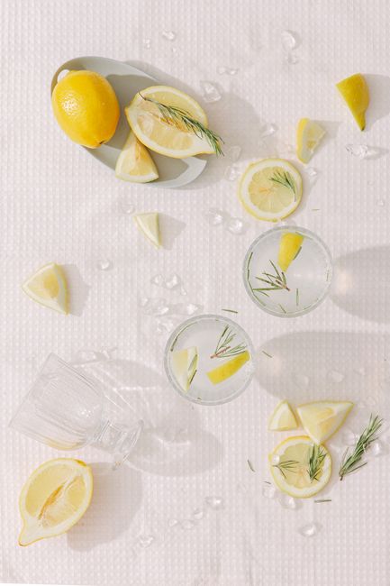 Top view of fresh lemonade with rosemary and ice cubes among sliced lemons on a white table.
