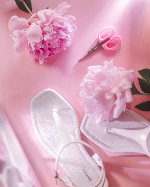 Chic arrangement with white sandals and vibrant pink peonies on a pastel pink background.