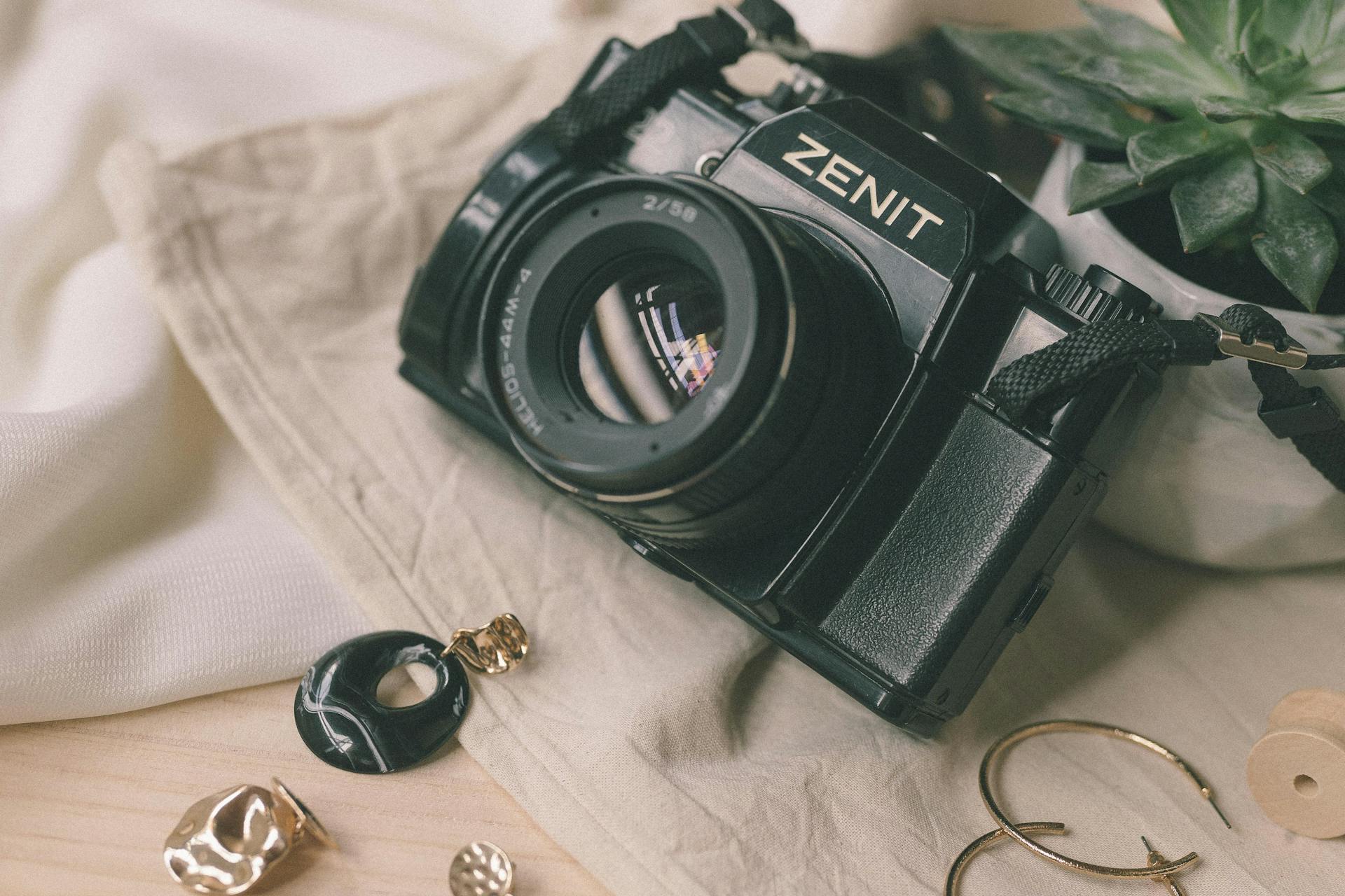 A vintage Zenit camera surrounded by jewelry and accessories on a soft fabric background.