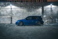 Side view of blue hatchback automobile placed on parking place with marking lines near cement barrier in city street in night time