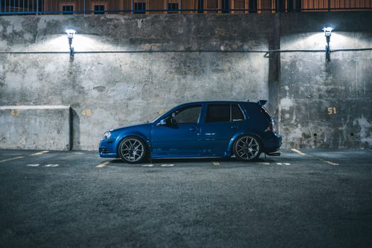 Side view of blue hatchback automobile placed on parking place with marking lines near cement barrier in city street in night time