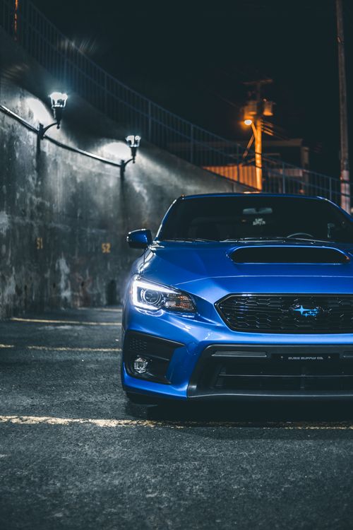 Free Contemporary blue car with body kit parked on parking space with marking near cement wall on street in night time Stock Photo