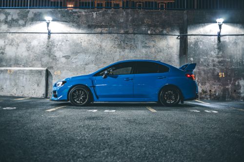 Free Side view of blue automobile with spoiler parked on street road near cement shabby wall on street in city at night Stock Photo
