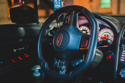 Black interior of contemporary automobile with steering wheel and illuminated dashboard with control panel in evening time with blurred street outside