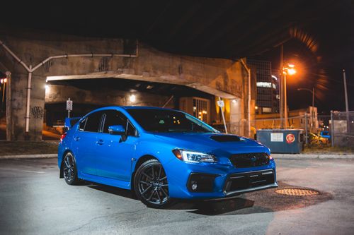 Free Contemporary blue automobile with headlights and spoiler parked on asphalt road near industrial building on city at night time outside Stock Photo
