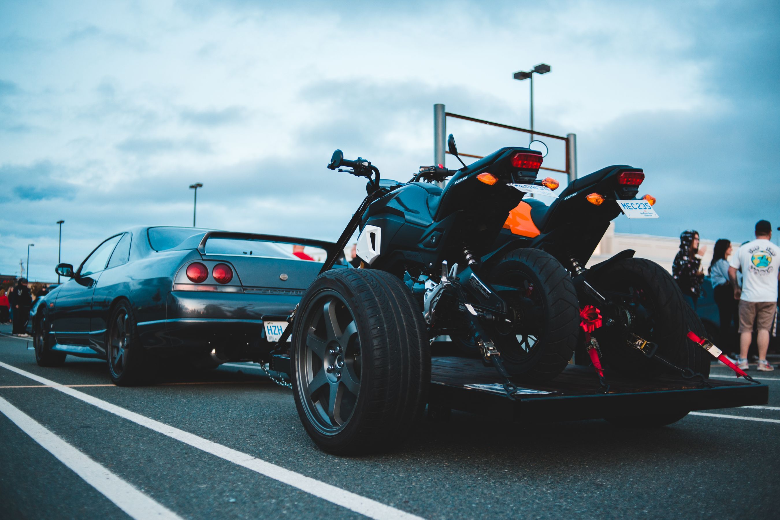 Black motorcycle secured on a flatbed trailer with red ratchet tie-down straps and soft loops on the front end