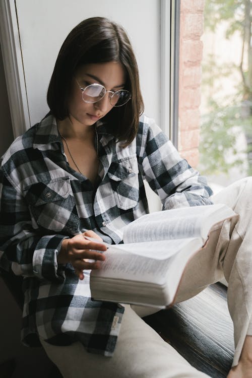 Free Woman in Black and White Plaid Dress Shirt Wearing Eyeglasses Reading a Book Stock Photo