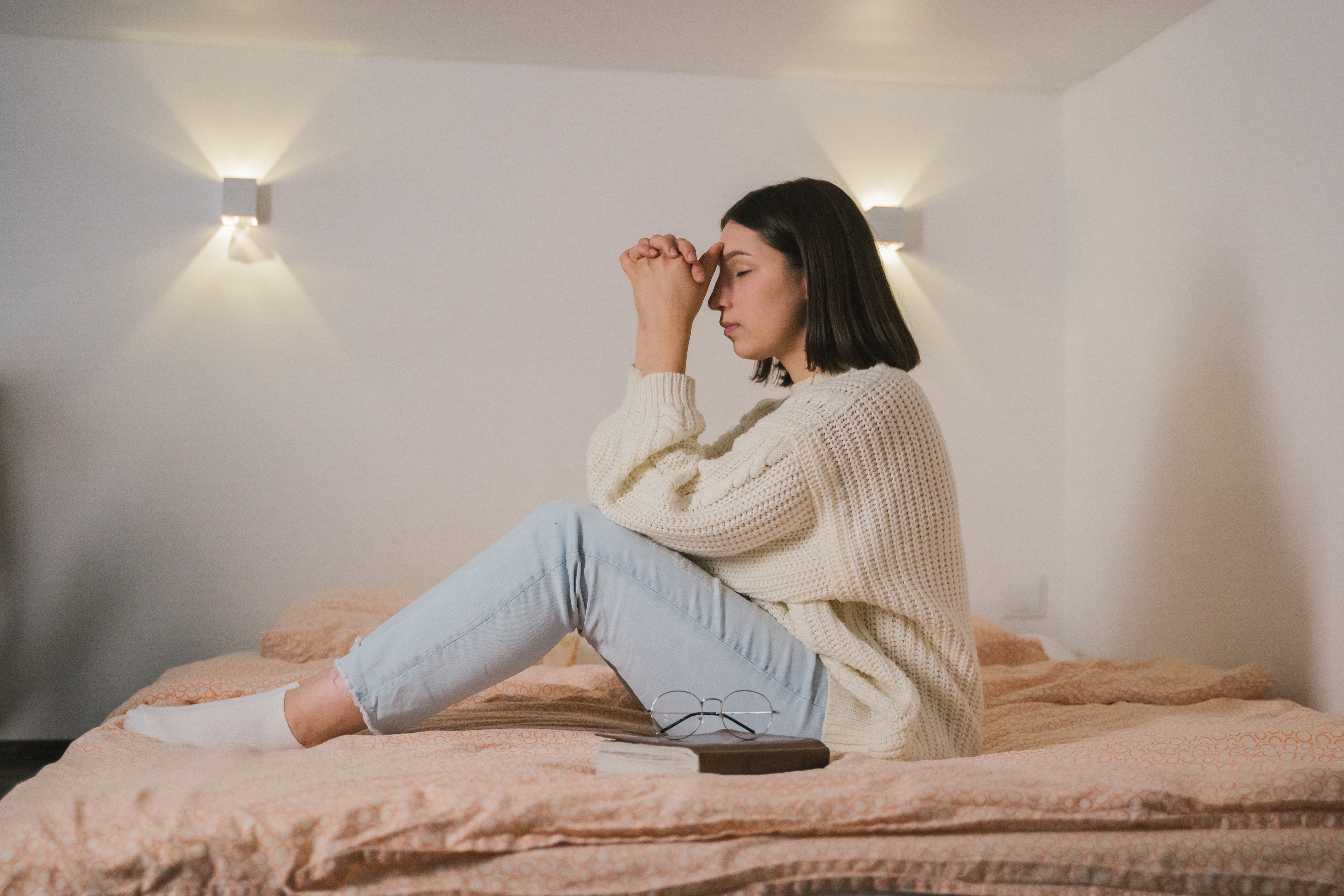 Woman in White Sweater Sitting and Praying on Bed · Free Stock Photo