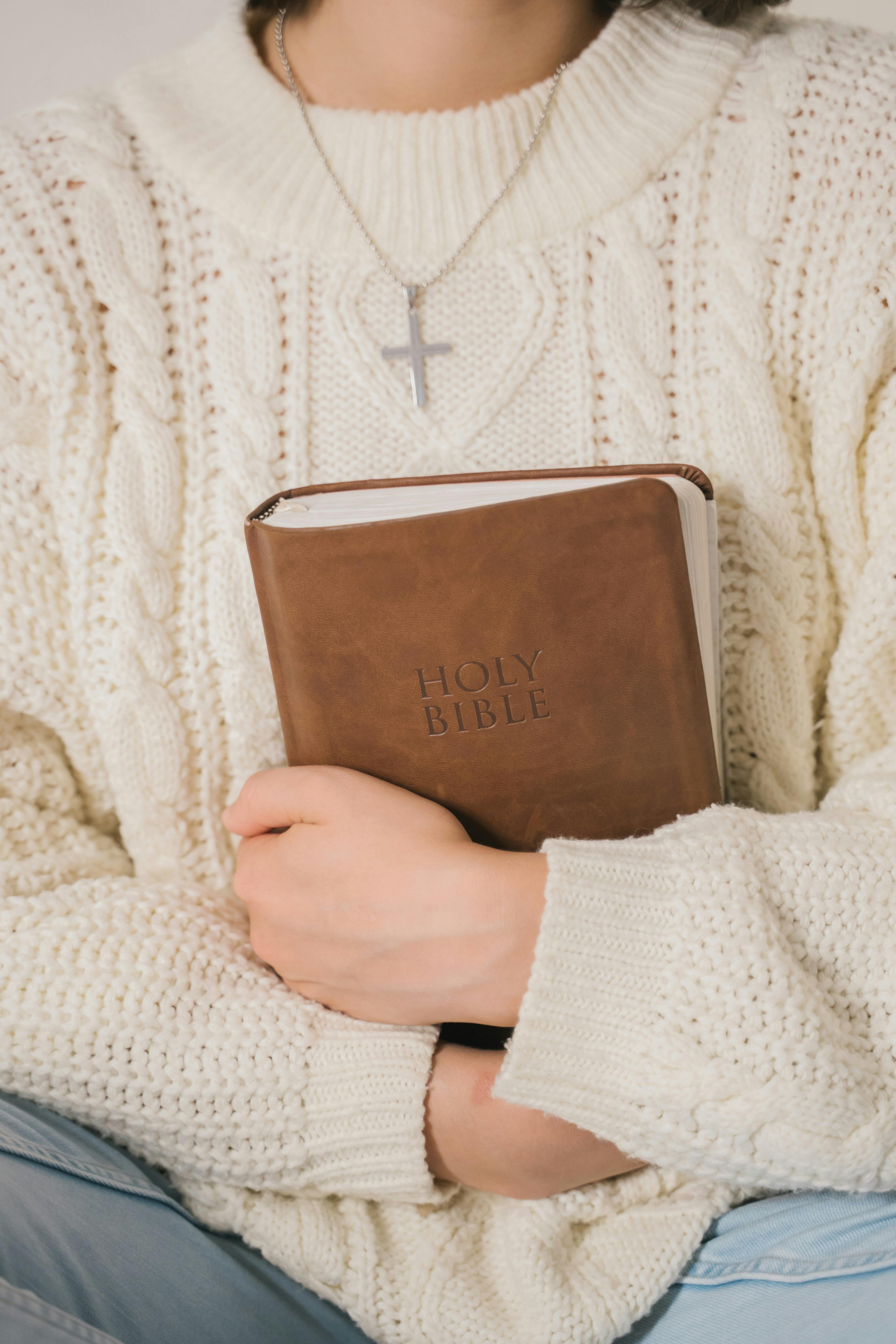 person in white sweater holding brown leather book