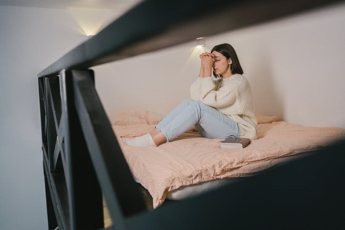 Free Woman in White Sweater and Blue Denim Jeans Sitting on Bed Stock Photo