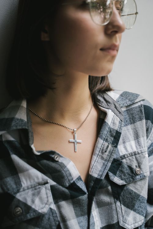 Free A close-up of a woman in glasses wearing a cross pendant necklace and plaid shirt indoors. Stock Photo