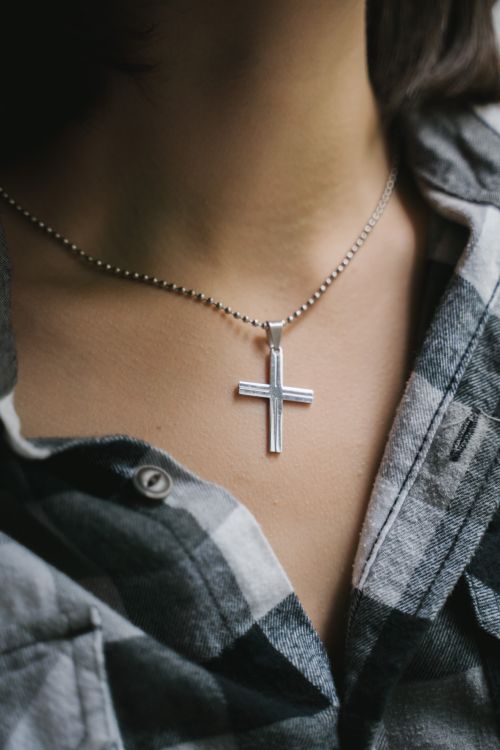 Free A close-up shot of a silver cross necklace worn by a person in a plaid shirt, symbolizing faith. Stock Photo