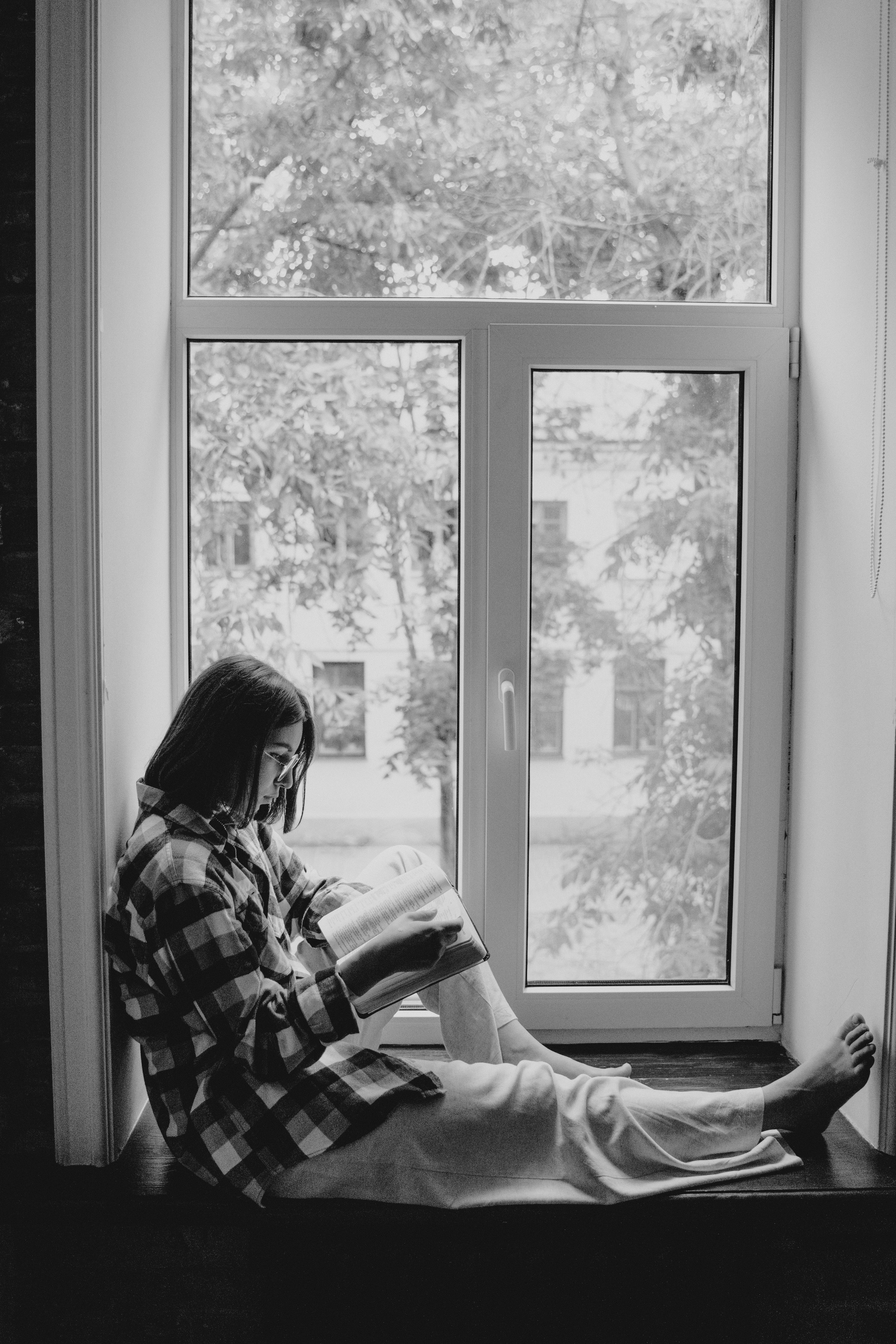 Woman reading a book while sitting on a windowsill in a monochrome setting.