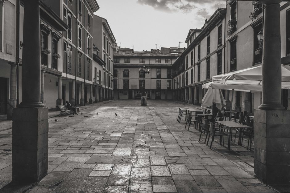 Vista en blanco y negro de una plaza histórica con mesas de café vacías en Oviedo, España.