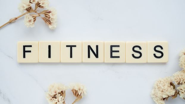 Close-up of scrabble tiles spelling 'FITNESS' on a marble surface with white flowers.