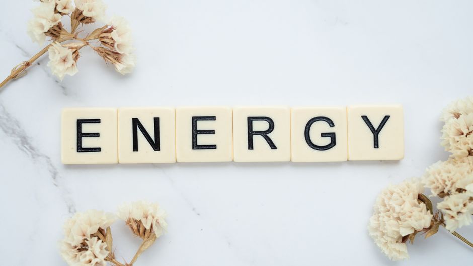 Close-up of 'Energy' spelled with Scrabble tiles on a marble surface with delicate white flowers.