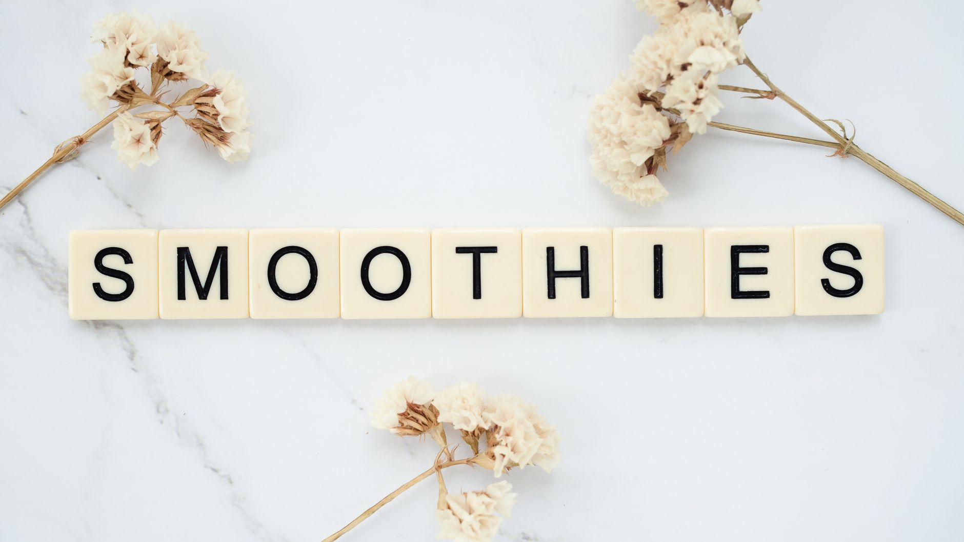 Des tuiles de Scrabble épelant 'Smoothies' sur une surface en marbre avec des accents floraux. Parfait pour un contenu de style de vie.