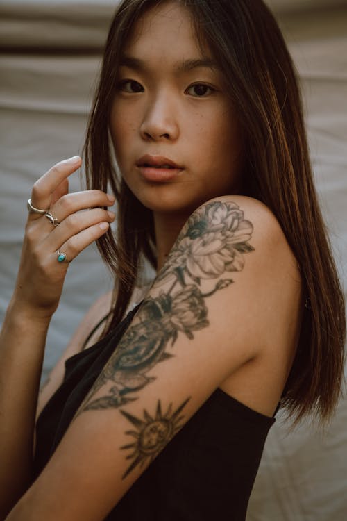 Side view of young Asian female with creative tattoo and rings on hand looking at camera
