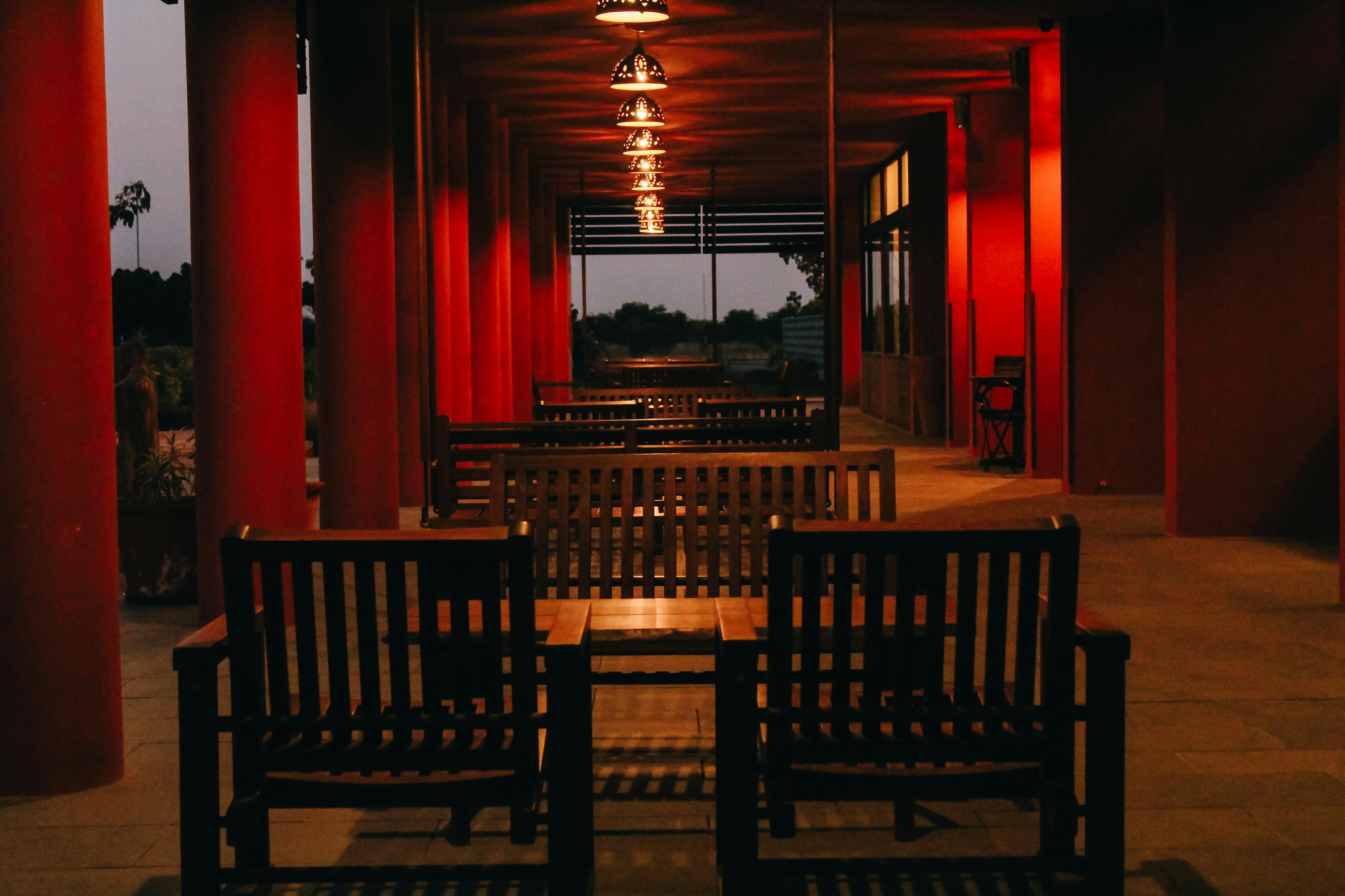 Red wooden columns supporting a covered deck underglow with concealed LED strips, producing an inviting glow that highlights architectural beams subtly.