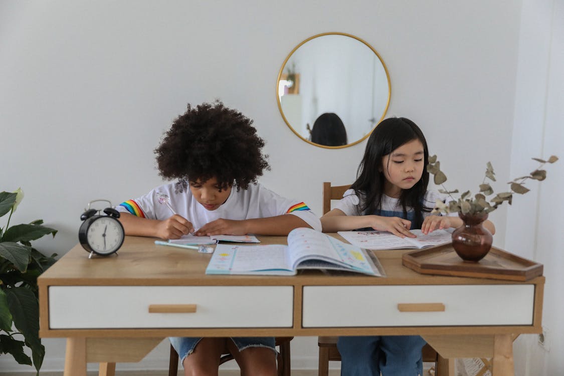 Concentrated multiracial girls sitting at table with notebooks and doing homework in cozy room
