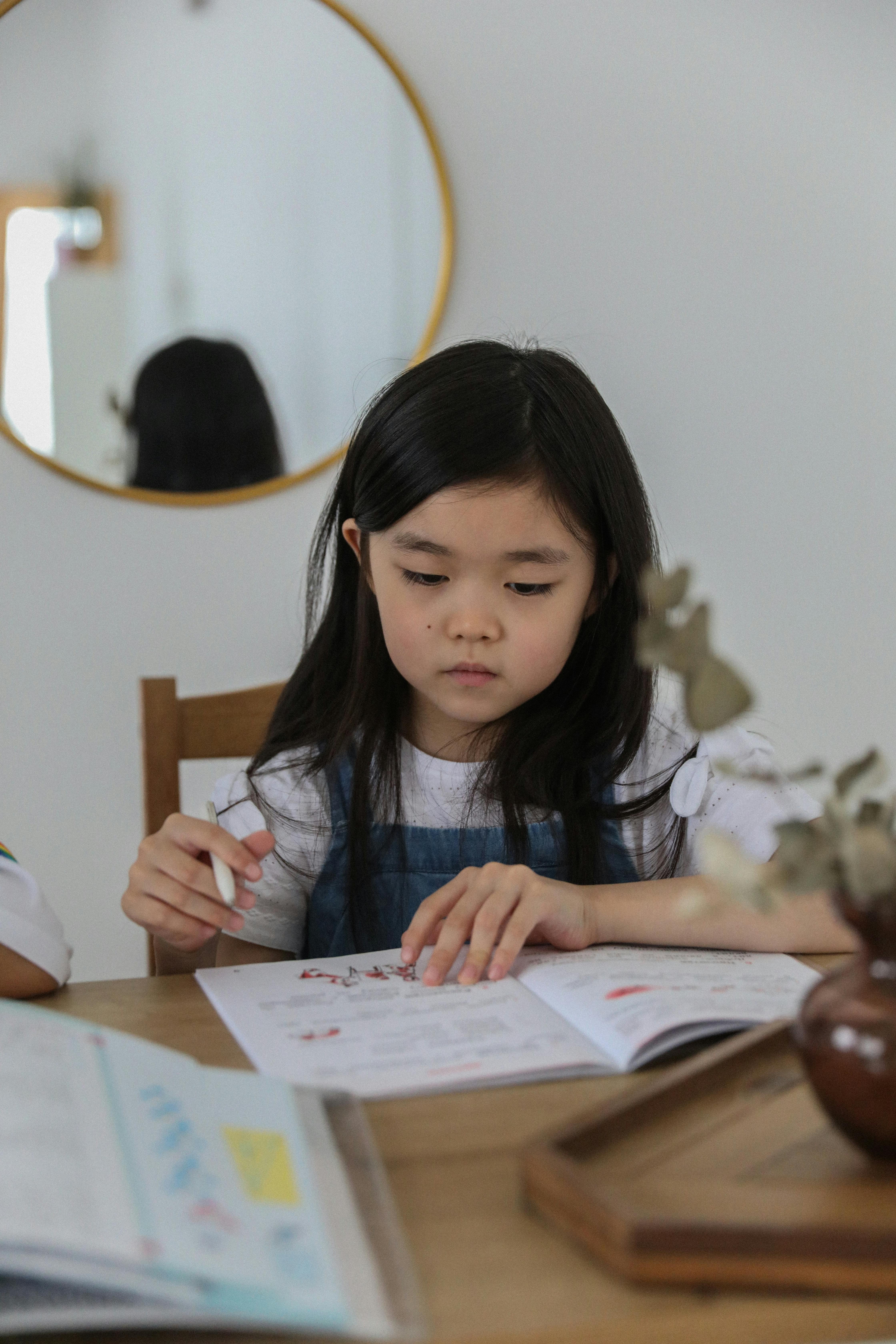 A thoughtful Asian girl concentrated on her homework at a cozy table indoors.