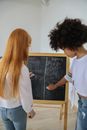 Multiethnic girls writing mathematical equations on chalkboard