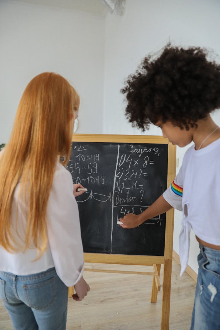 Multiethnic Girls Writing Mathematical Equations On Chalkboard