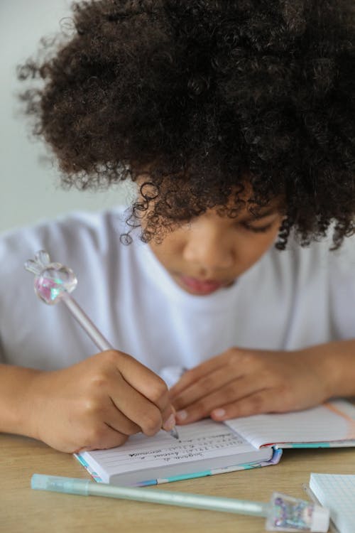 Free Crop African American schoolgirl writing in diary at desk Stock Photo