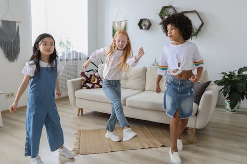 Happy multiethnic girlfriends dancing on floor at home