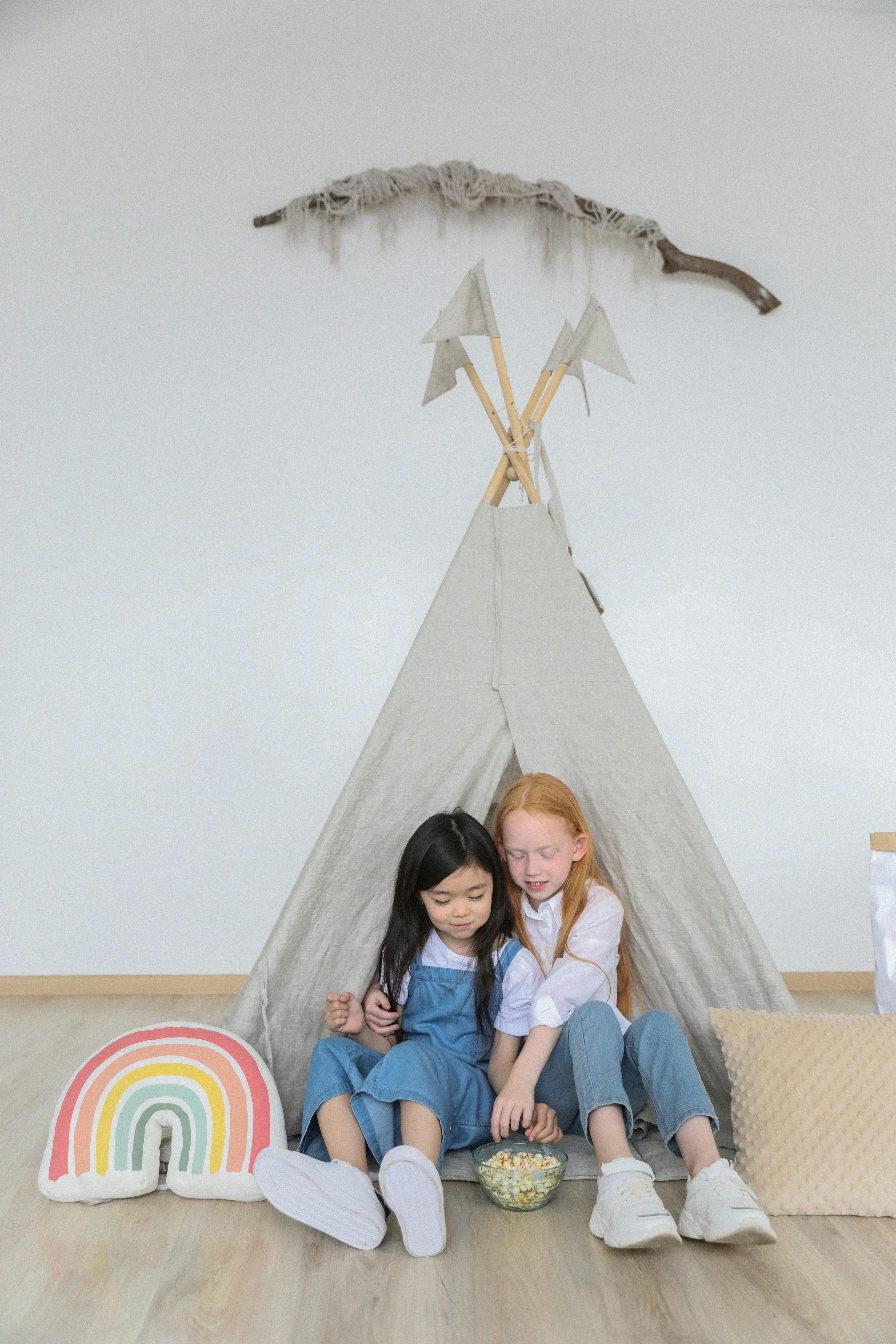 multiracial girlfriends with popcorn near play tent on floor