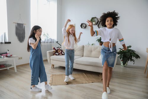 Content multiracial children dancing with raised arms on floor near sofa in living room