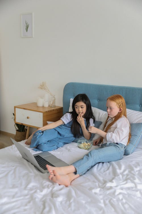 Multiracial girls watching movie on laptop while resting on bed