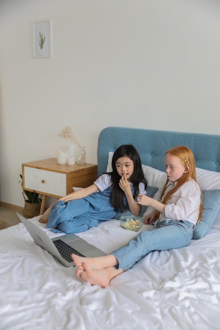 Multiracial Girls Watching Movie On Laptop While Resting On Bed