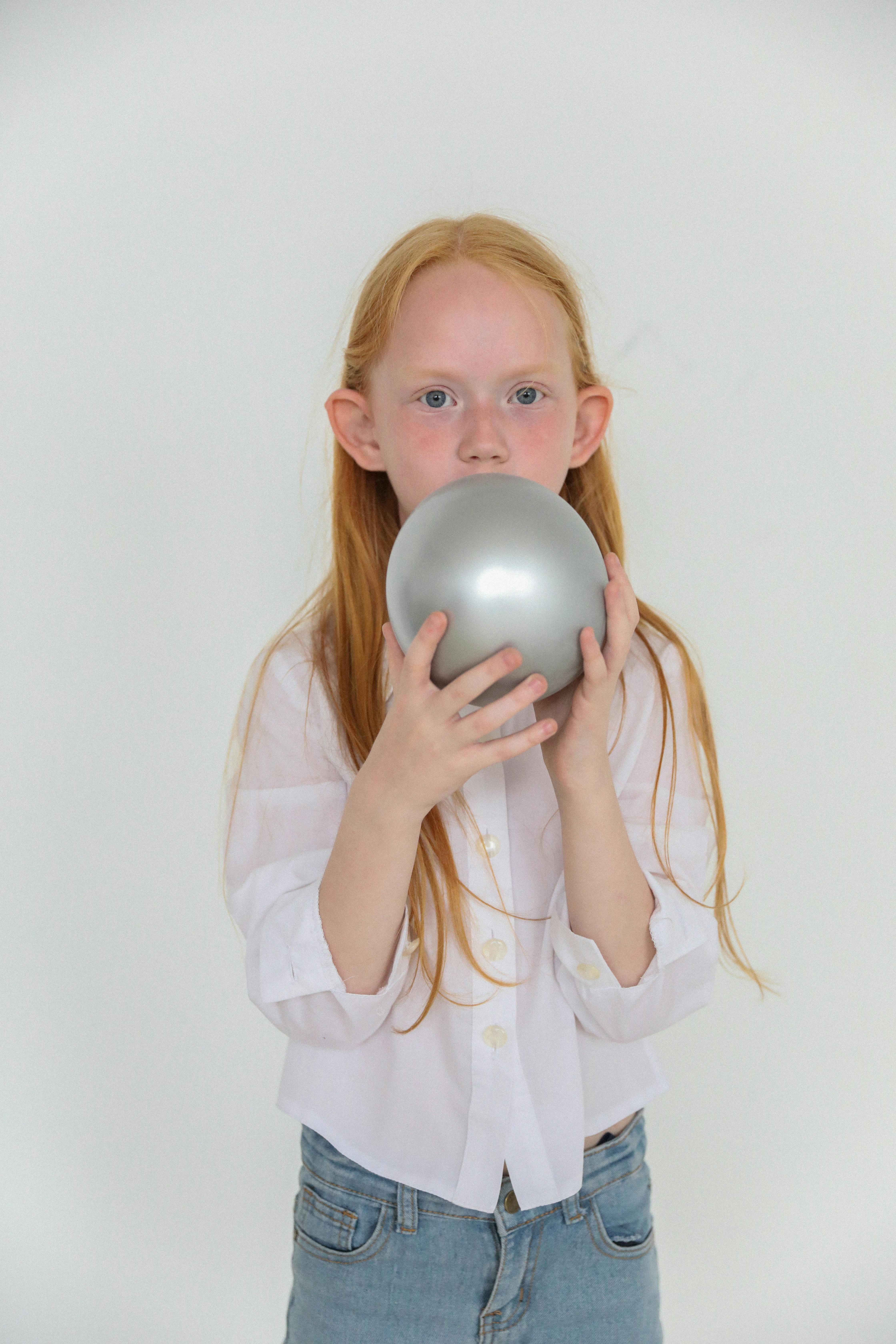 charming girl with red hair inflating gray balloon