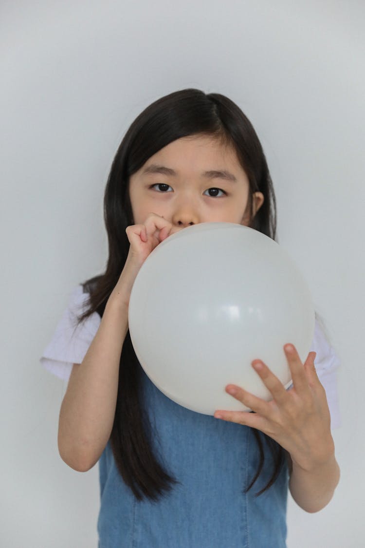 Cute Ethnic Child Inflating White Balloon In Studio