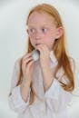Concentrated little redhead child blowing balloon in white studio