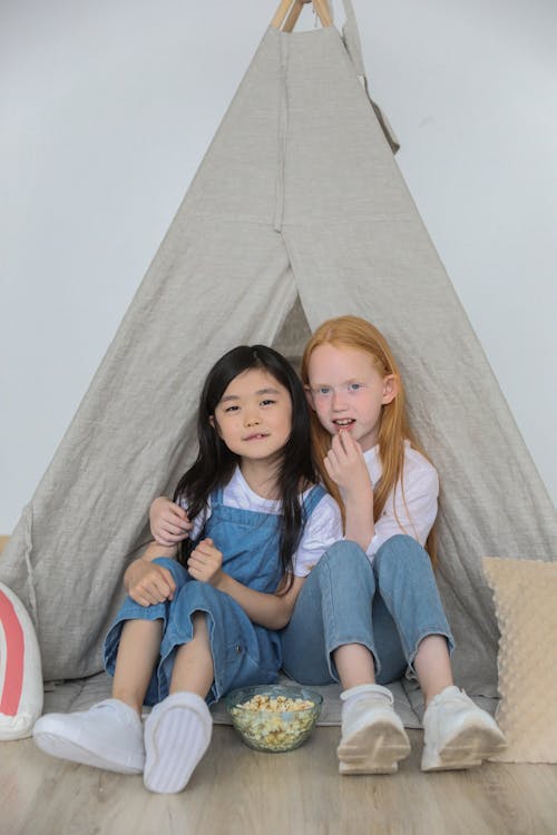 快樂的多樣小孩子在家裡的帳篷裡一起玩時擁抱和吃爆米花
