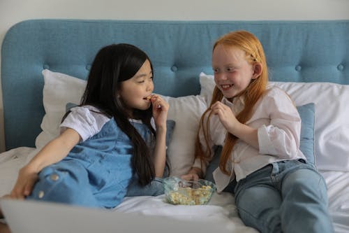 Gadis Kecil Yang Beragam Dan Positif Tersenyum Dan Makan Popcorn Di Tempat Tidur