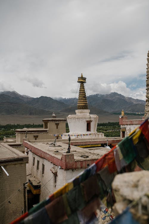 Roof of ancient temple with shabby walls with tower and hanging flags against cloudy sky and mountains in distance in town