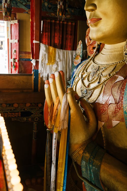 Free Golden sculpture of Buddha with ribbons on hands located in ancient palace near barrier with lightning candles in traditional style Stock Photo