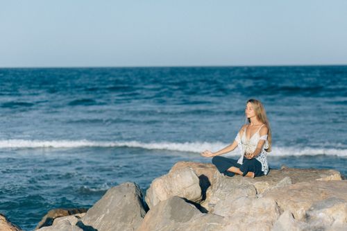 Free A woman practices meditation outdoors on rocks by the sea, embodying tranquility and relaxation. Stock Photo