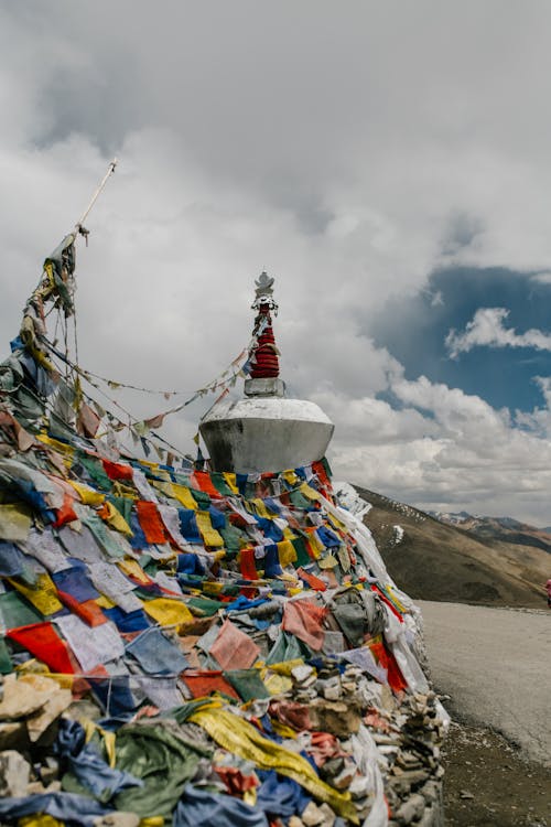 Wall of colorful flags hanging near stone tower of ancient monastery located in mountainous area against cloudy sky in nature in town