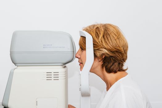 A woman undergoing an eye exam with an autorefractor in a clinical setting.