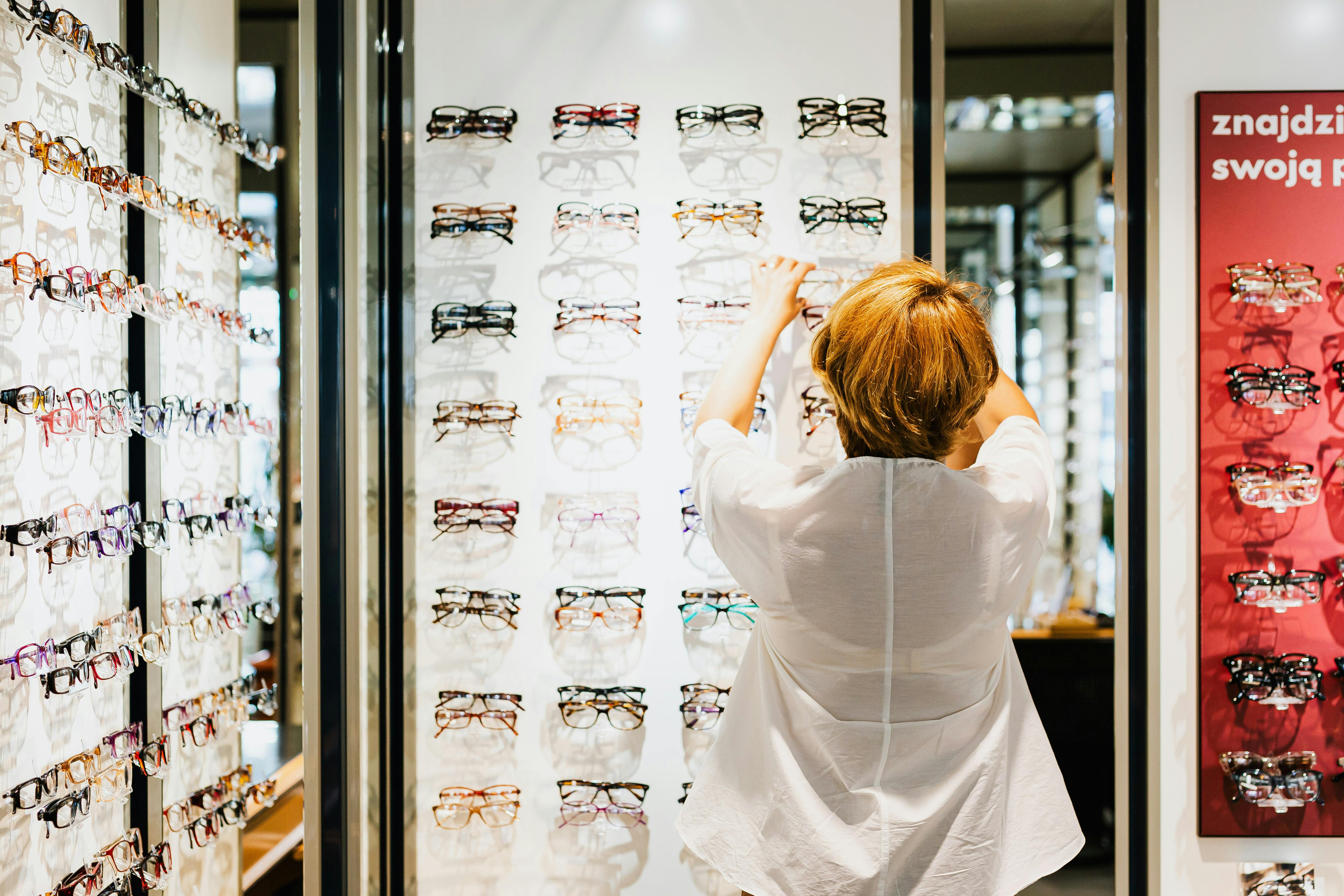 a woman in white blouses looking at the eyeglasses on the shelves