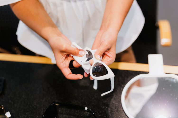 A Hand Wiping The Lens Of The Sunglasses