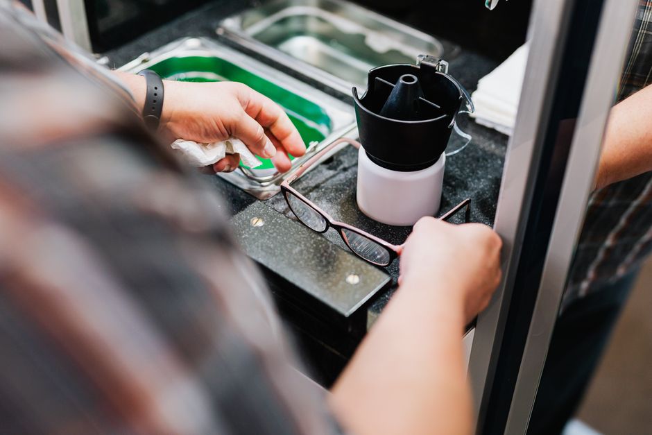 Close-up of hands cleaning eyeglasses at an optical workstation. Ideal for eyewear, optician, and cleaning themes.