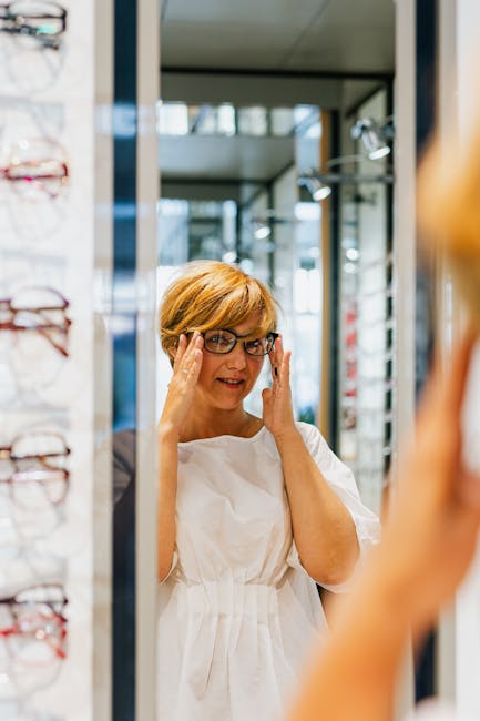 Adult woman trying on eyeglasses at an optical store, looking in a mirror.